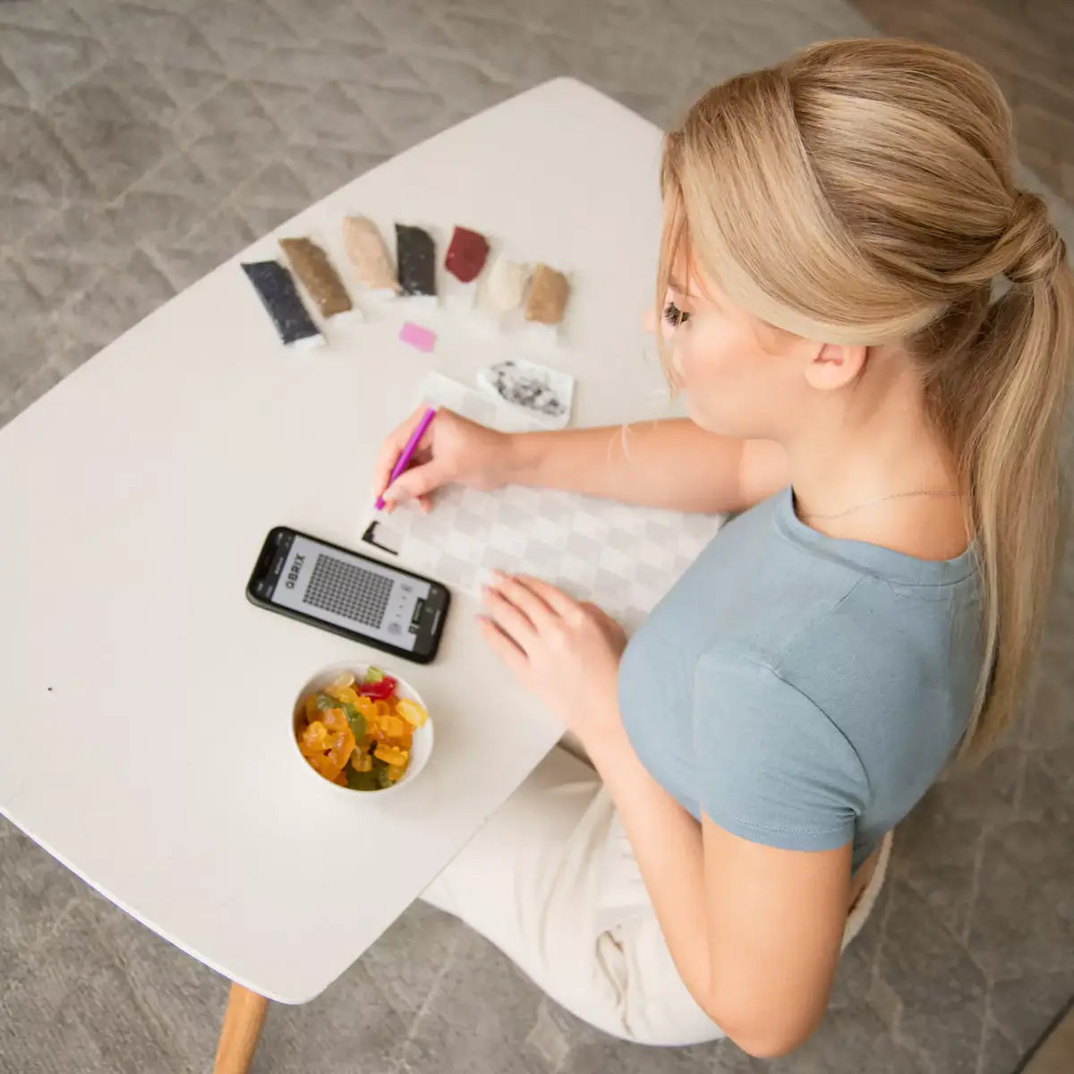 Woman sitting at a table with a phone, color swatches, and a snack.